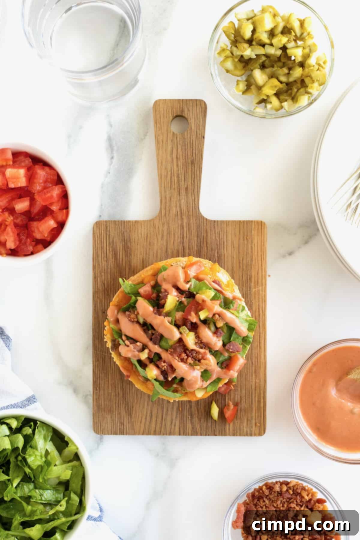 A fully assembled and garnished cheeseburger bun pizza on a small wooden cutting board, ready to eat.