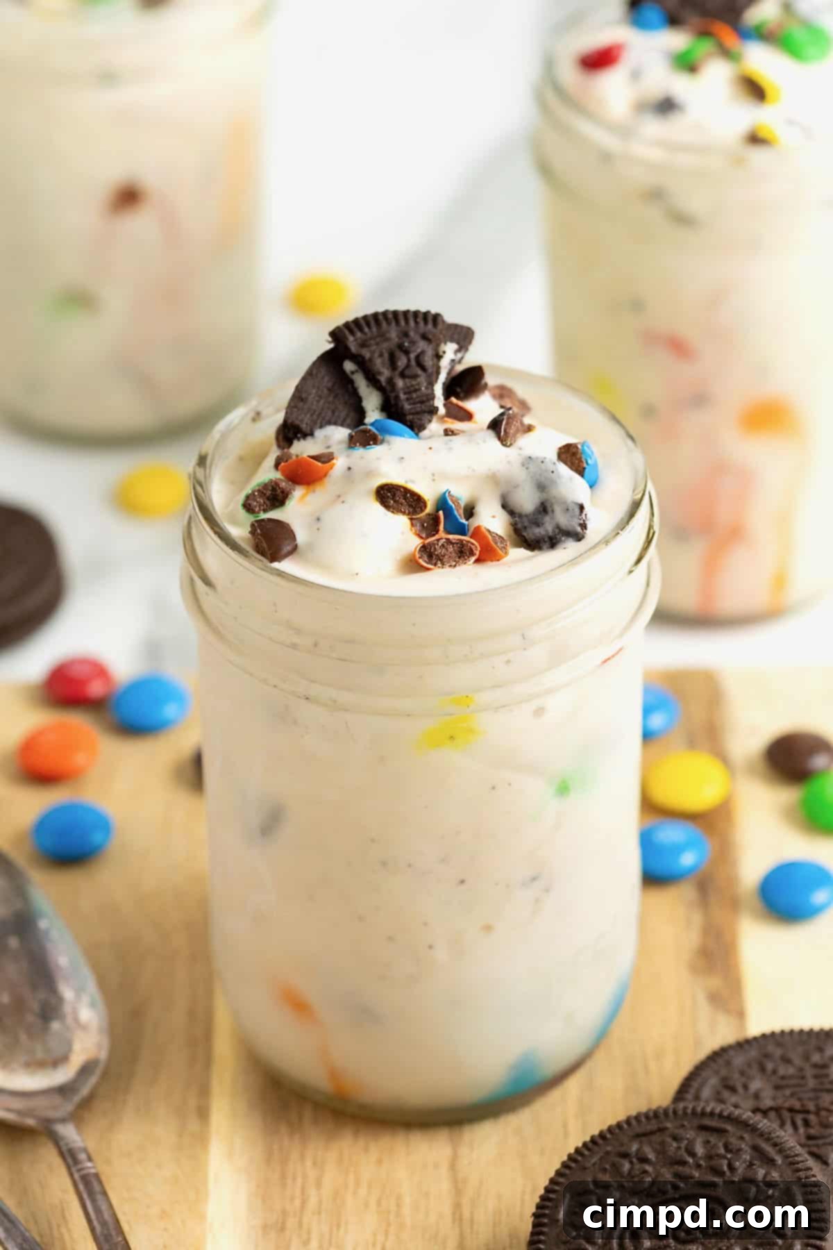 A homemade M&M Blizzard garnished with a piece of Oreo in a wide mouth jar, on a rustic wooden surface, inviting indulgence.