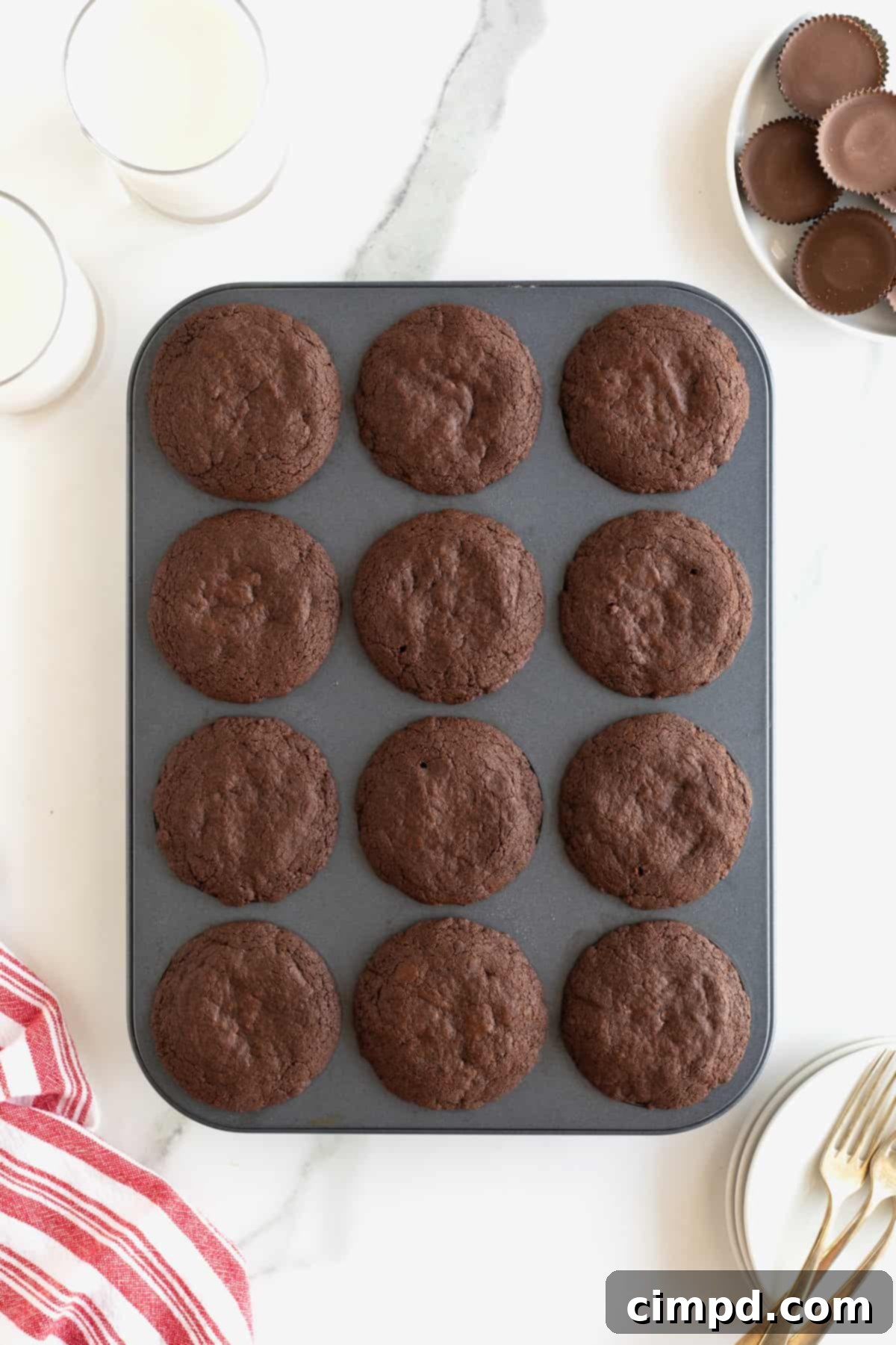 Baked brookies in a dark metal 12-cup muffin pan on a white counter, cooled and ready.