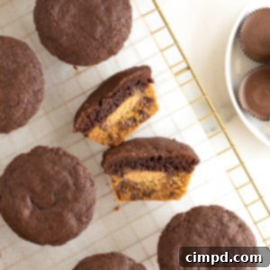 A muffin-shaped treat with a cookie bottom, a brownie top and a peanut butter cup in the middle cut in half laying on a parchment lined cooling rack.