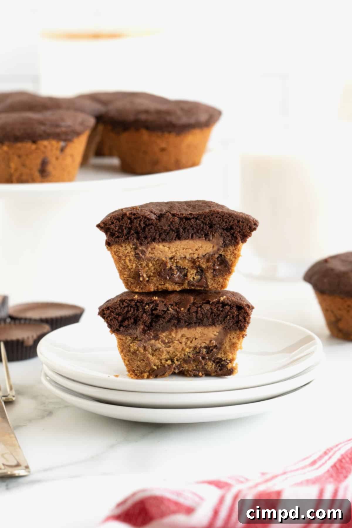 Two brookies stacked on top of each other on top of a small white plate. The brookies are cut in half to reveal a peanut butter cup inside, showcasing the layered beauty.