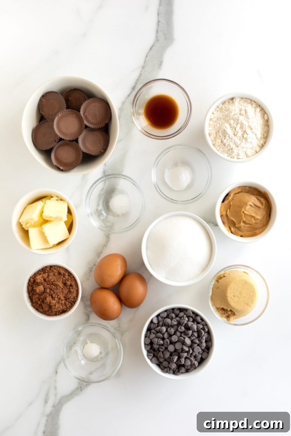 Ingredients for peanut butter cup stuffed brookies in small glass containers on a white marble counter, neatly organized.