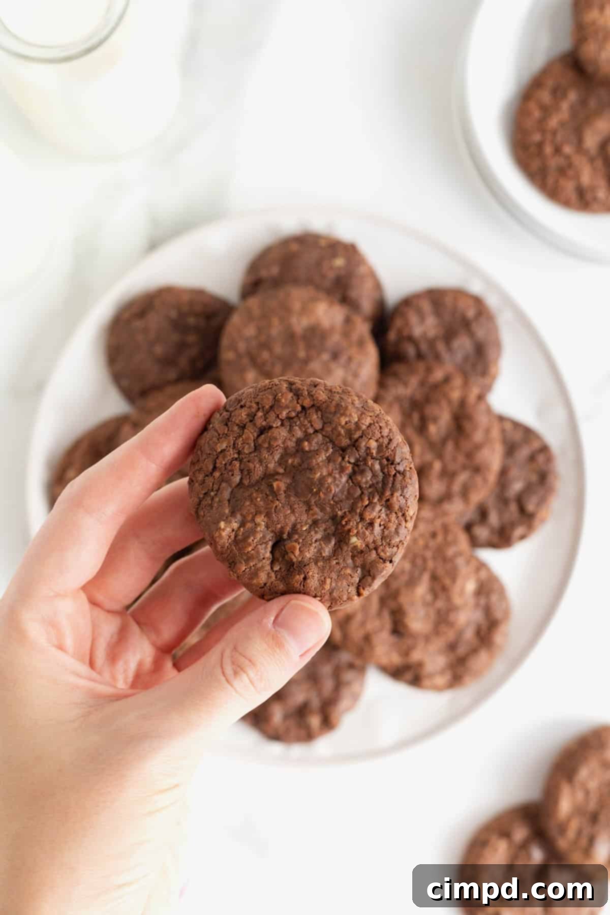 A hand holding a Nutella cookie over a large white plate 