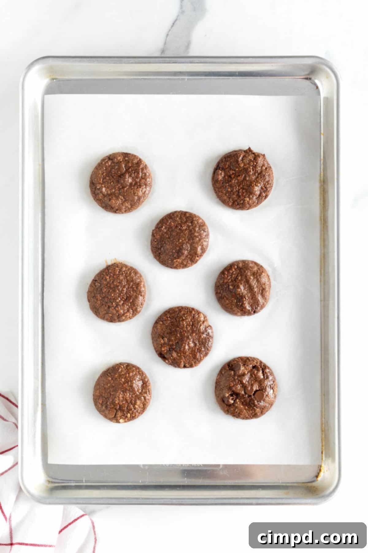 Eight Nutella cookies on a parchment lined aluminum baking sheet.
