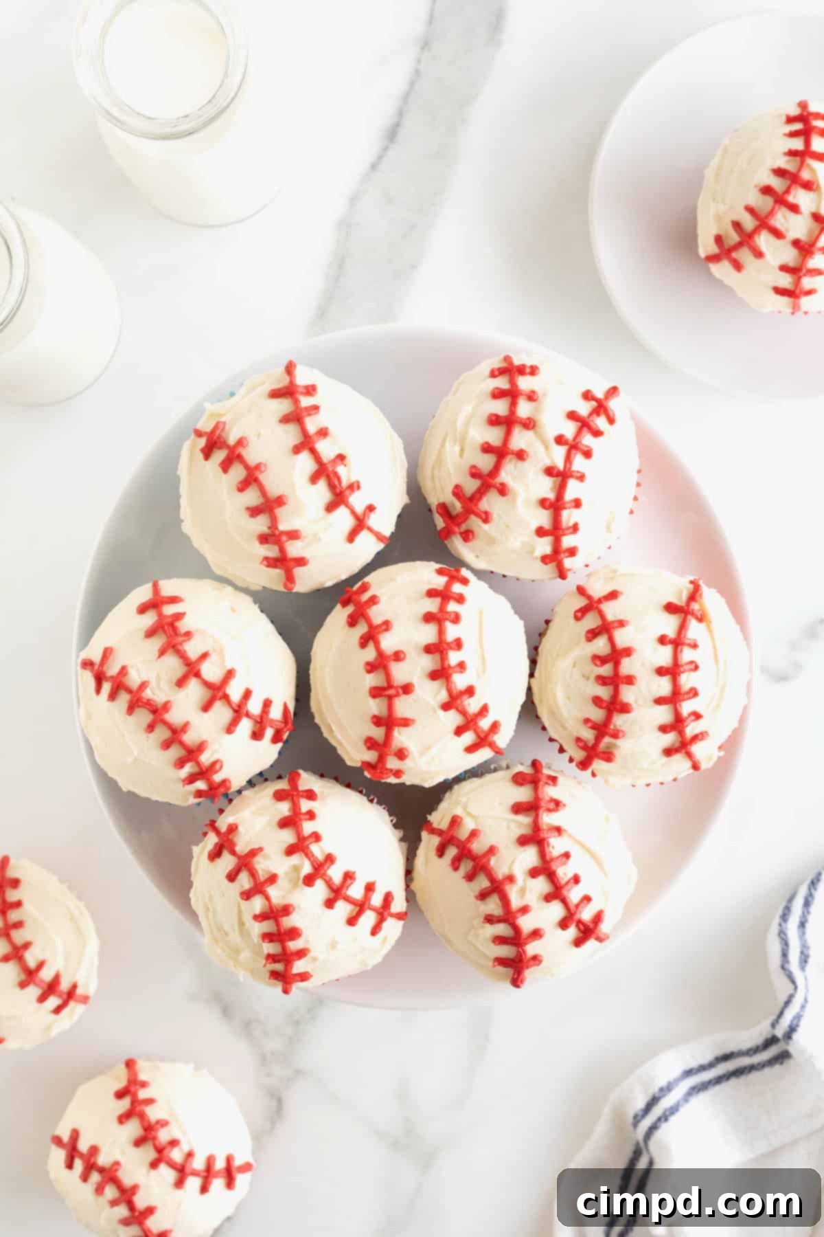 A large round white plate filled with beautifully frosted baseball cupcakes, ready for a party.