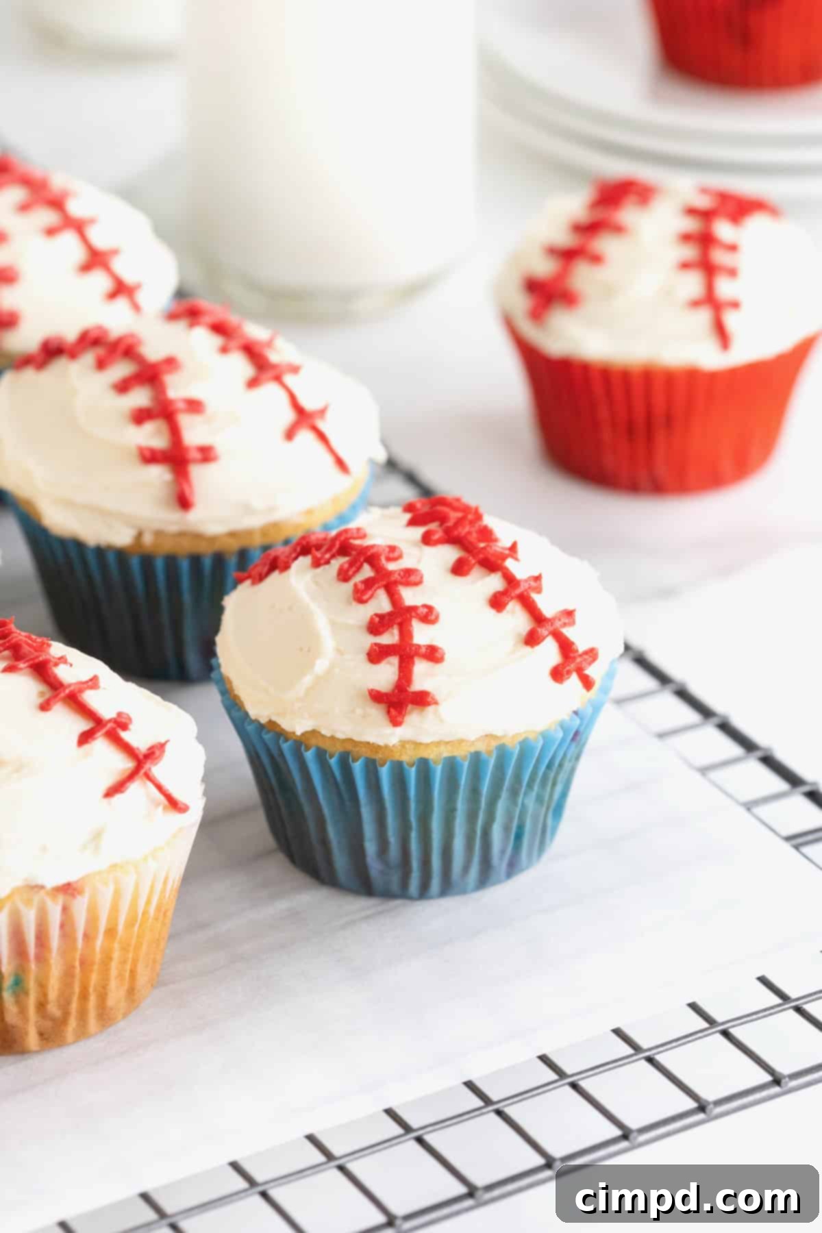 Four perfectly frosted baseball cupcakes resting on a parchment-lined cooling rack, ready to be enjoyed or stored.
