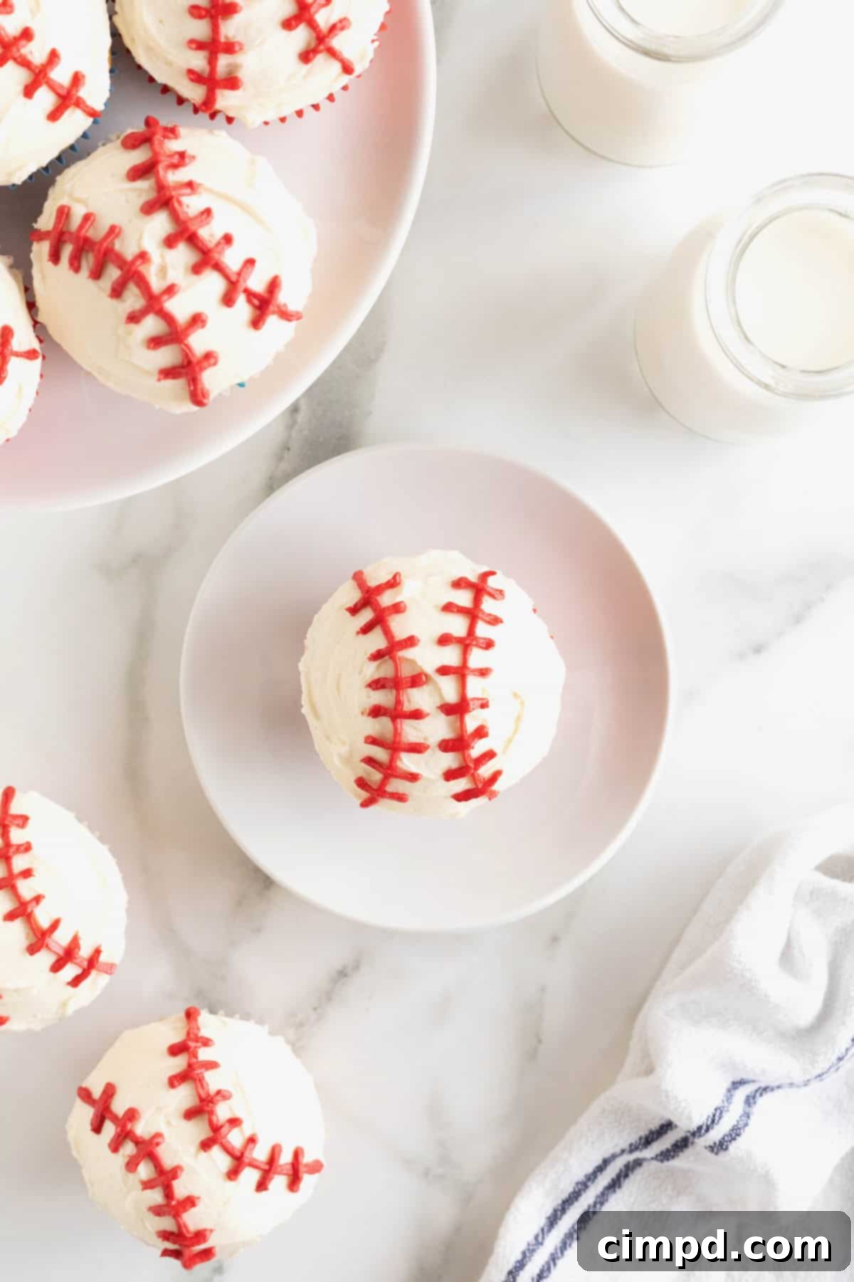 A single beautifully decorated baseball cupcake resting on a small white-rimmed plate on a sleek white marble counter.