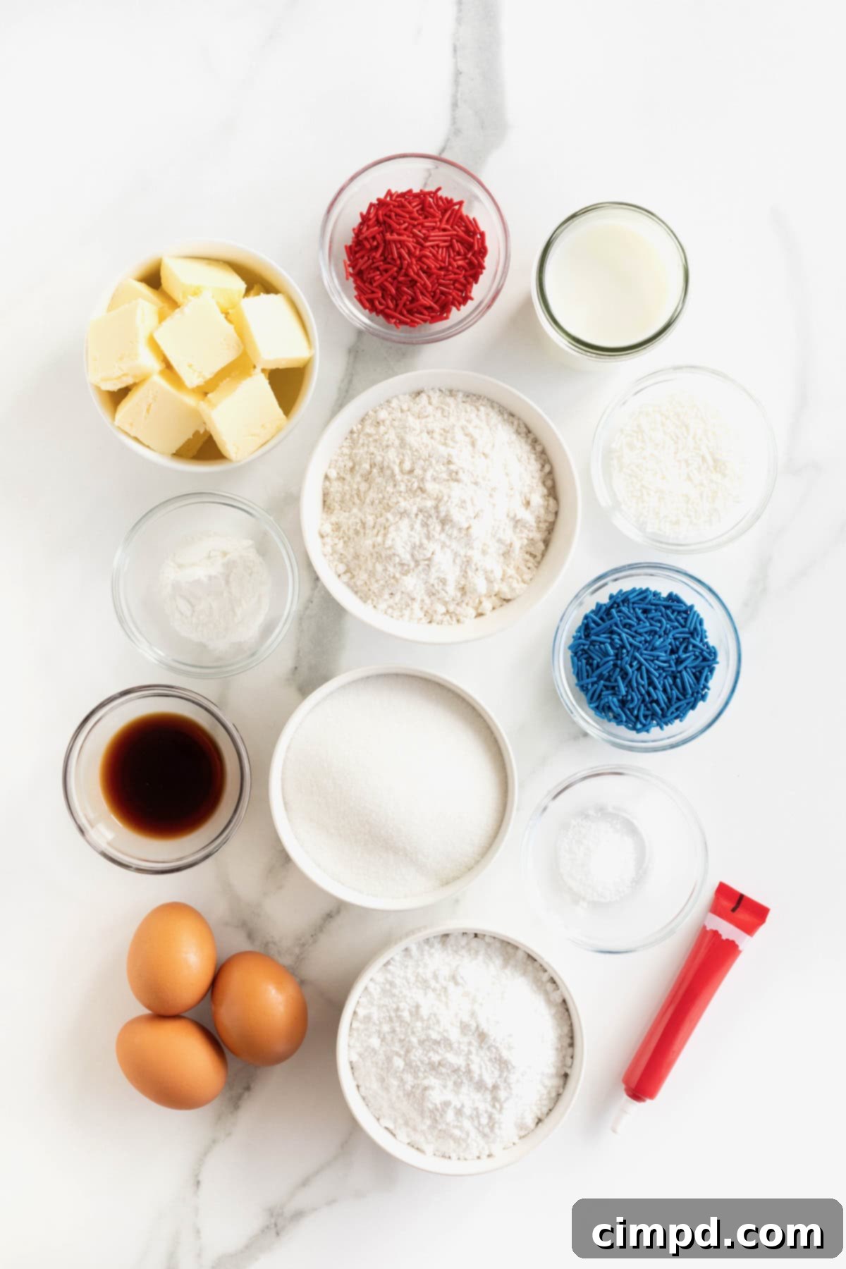 A collection of ingredients for confetti baseball cupcakes, neatly arranged in small glass dishes on a white marble countertop, awaiting preparation.