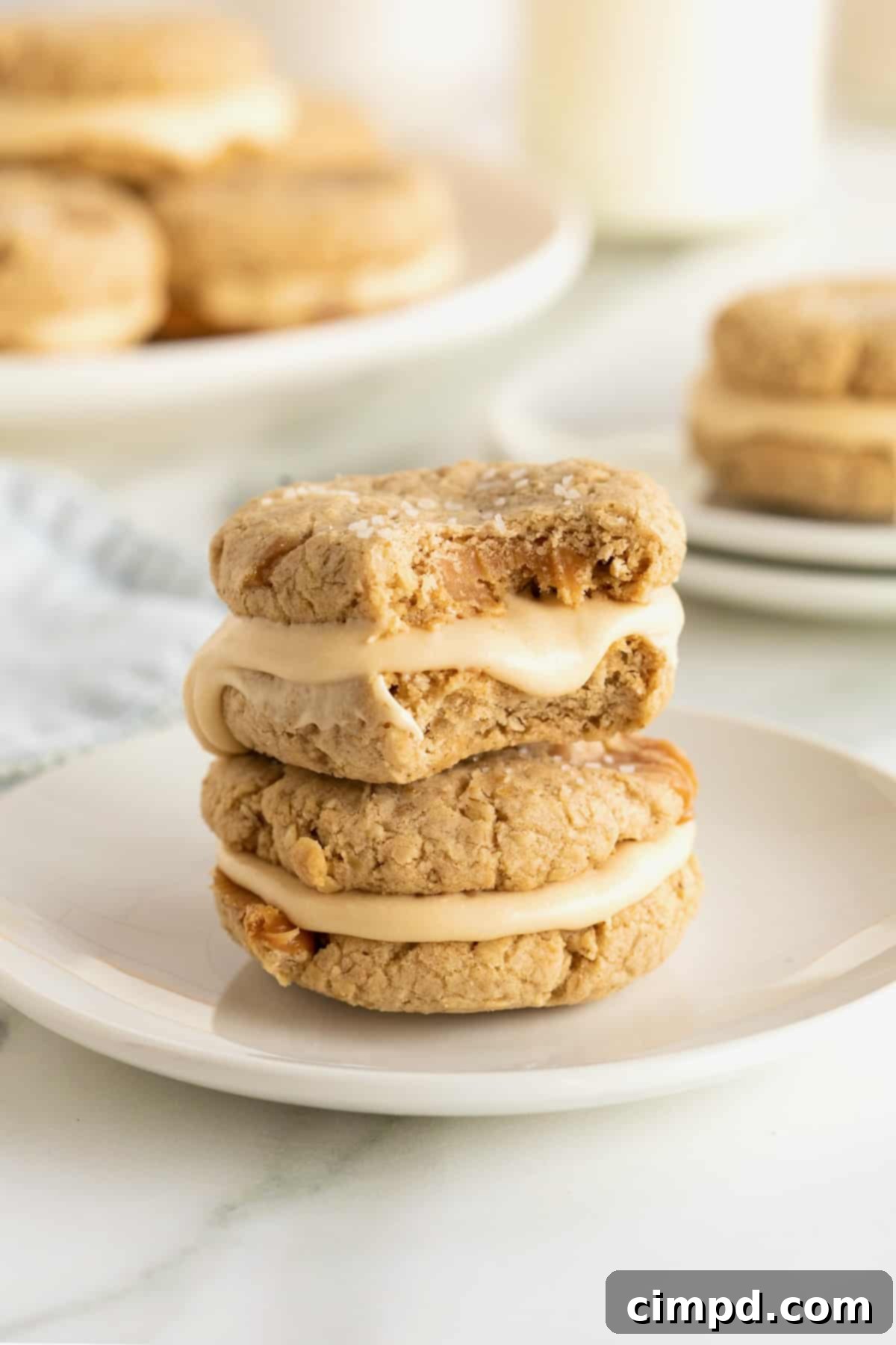 Irresistible Salted Caramel Oatmeal Cream Pies 3 Two delicious salted caramel oatmeal cream pies stacked on a white plate, with the top pie revealing a bite taken out, showing the luscious filling.