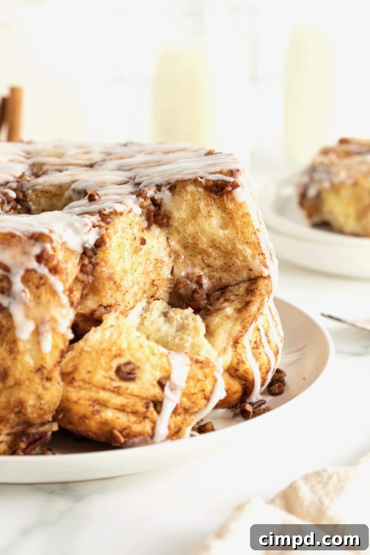 Easy Overnight Sweet Rolls 2 Sweet rolls topped with a white glaze and chopped nuts on a large white serving plate.