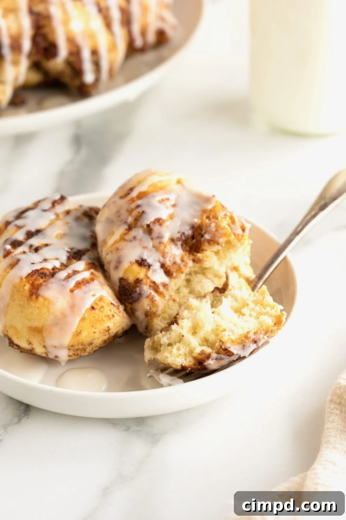 Easy Overnight Sweet Rolls 3 Two sweet rolls covered in glaze and chopped pecans on a white plate with a fork.