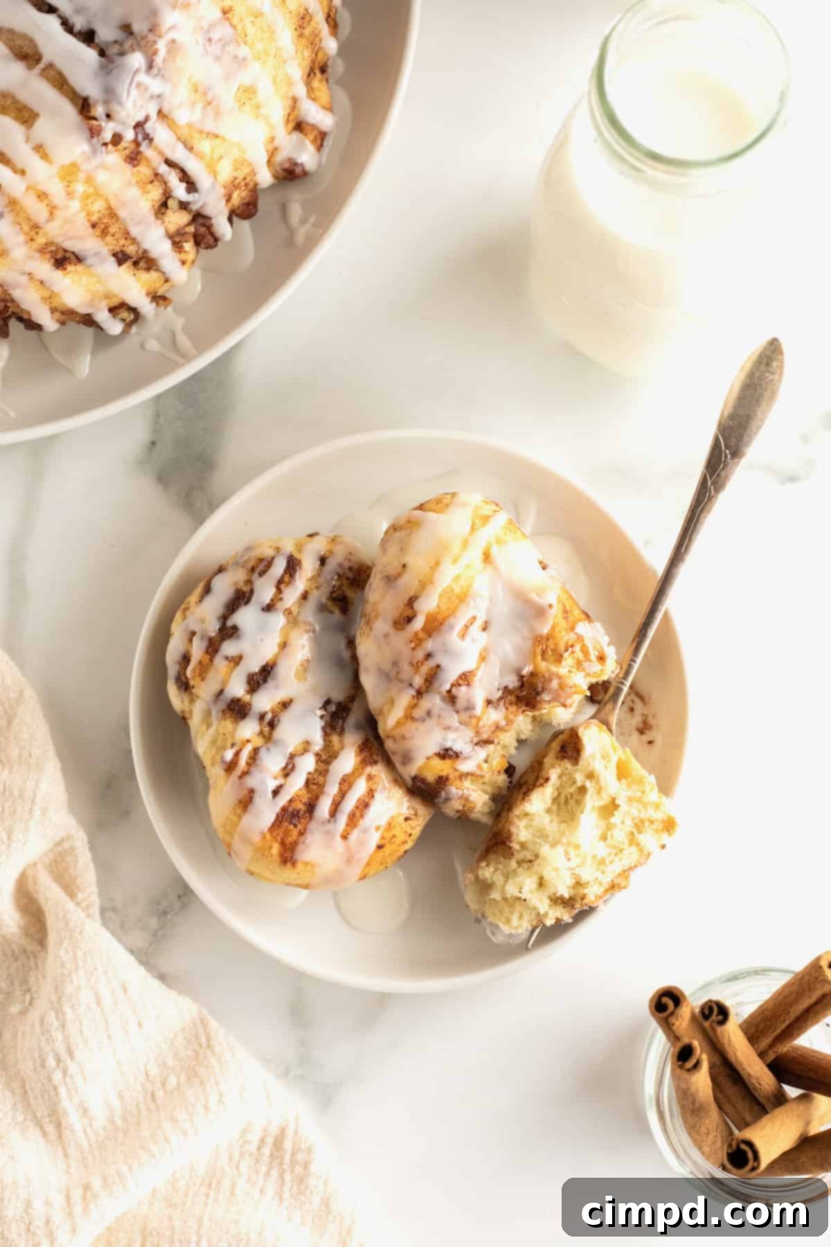 Easy Overnight Sweet Rolls 6 Two sweet rolls covered in glaze and chopped pecans on a white plate with a fork.