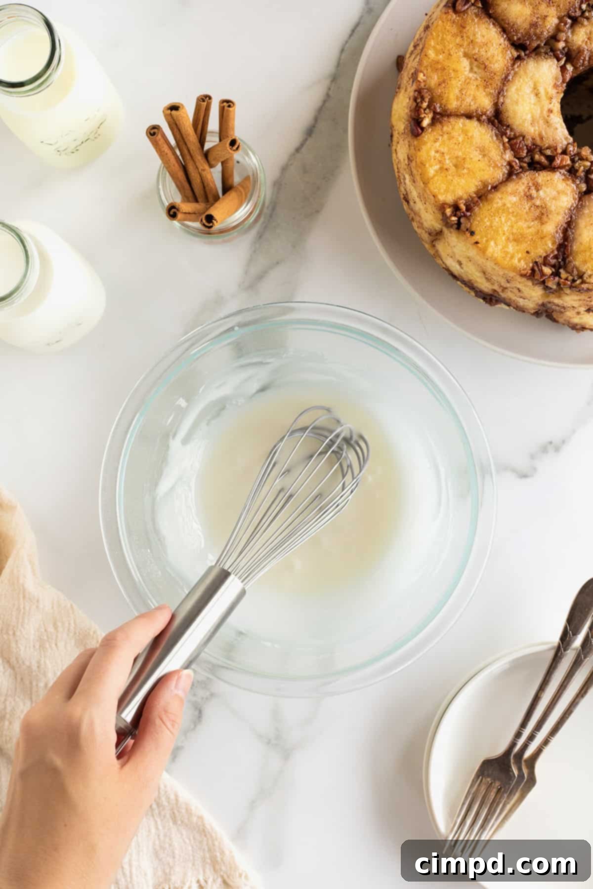 Easy Overnight Sweet Rolls 10 A hand holding a whisk in a small glass bowl of white glaze.
