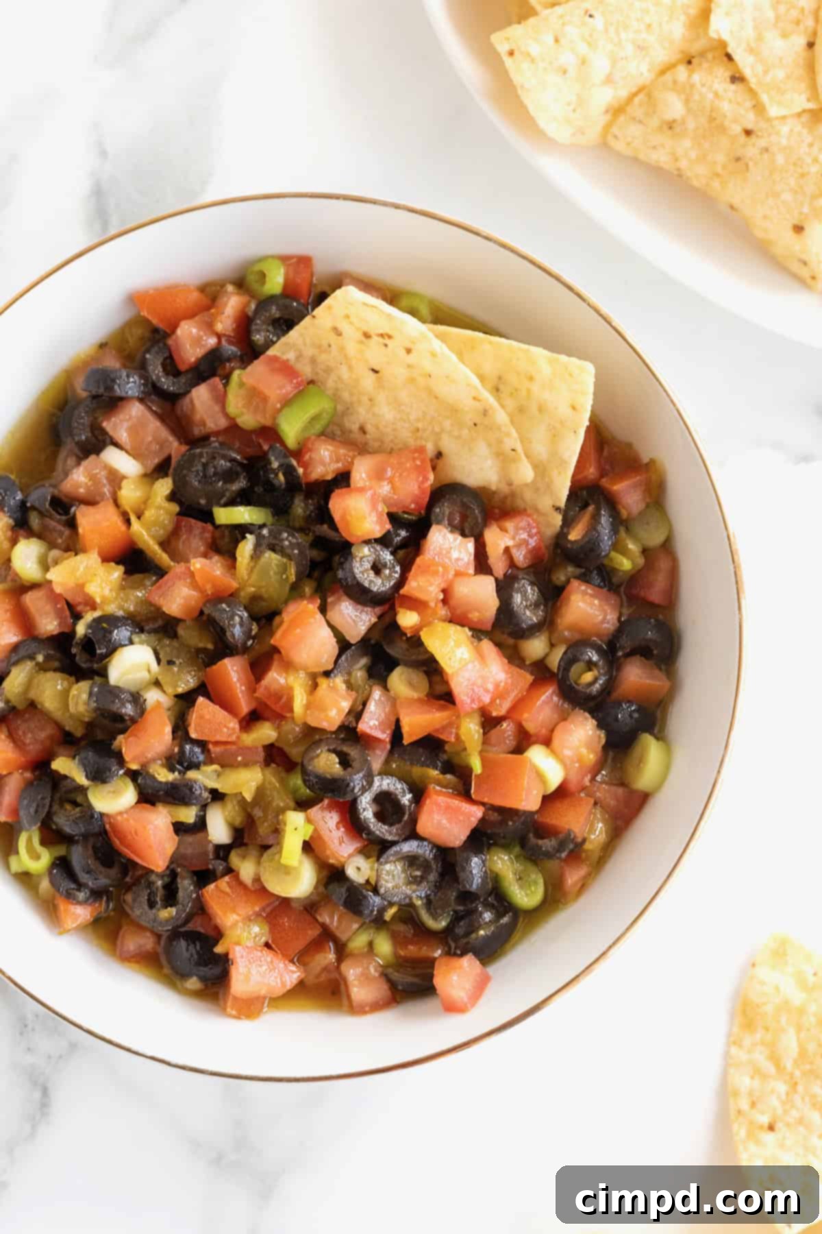 A large white serving bowl with a gold rim filled with colorful harlequin dip, ready to be served.