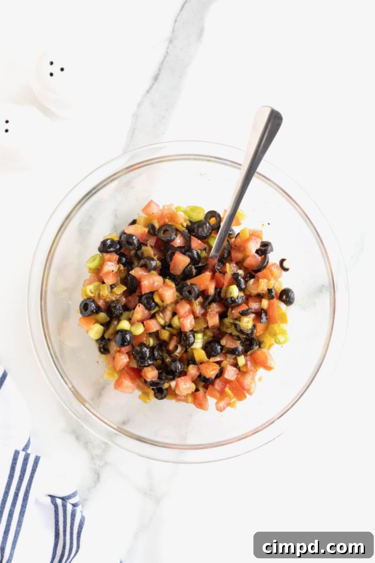 A large glass serving bowl filled with Harlequin Dip, with a metal spoon resting inside, ready for dipping.