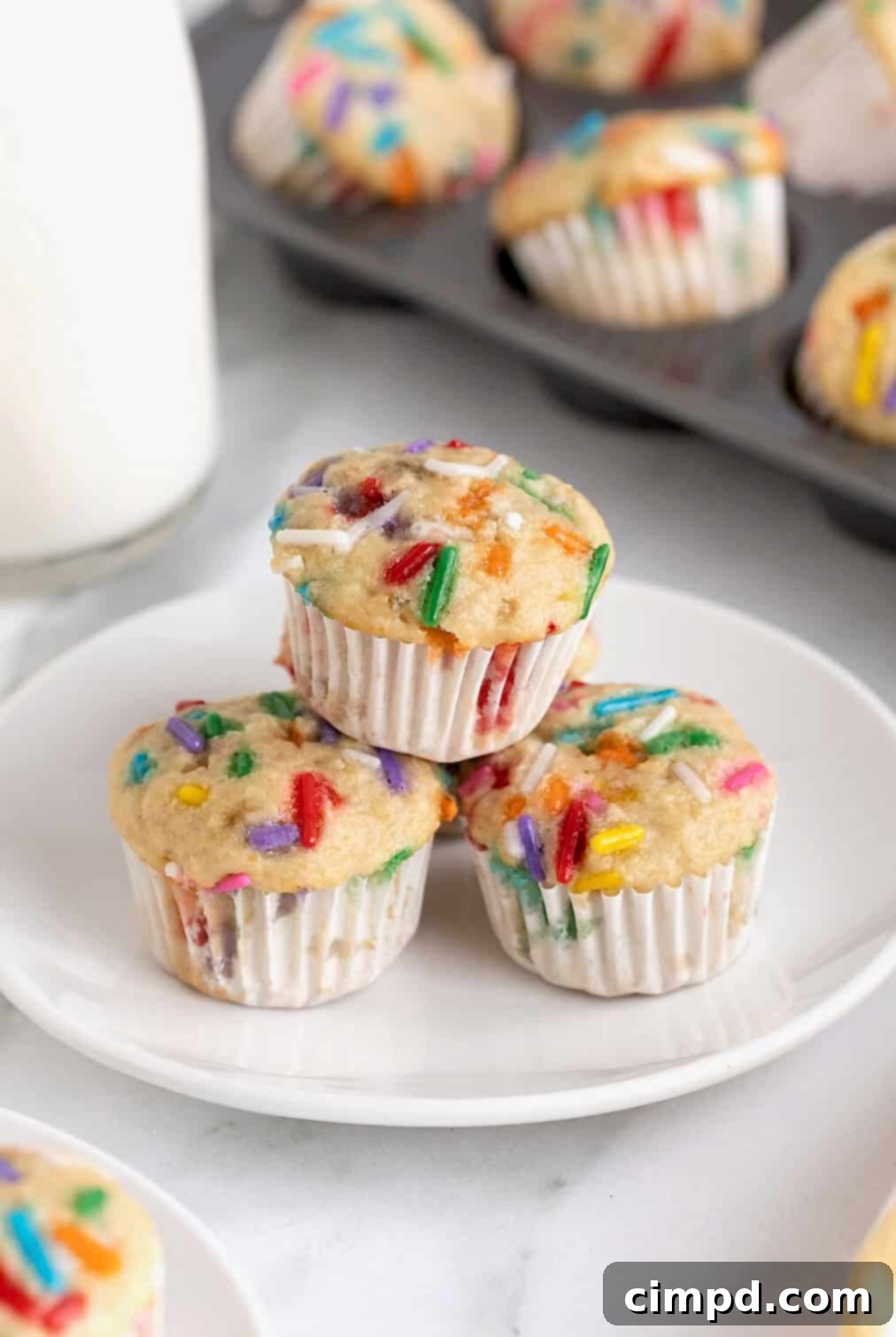 Three birthday breakfast muffins with colorful sprinkles on a white plate, ready to be enjoyed.