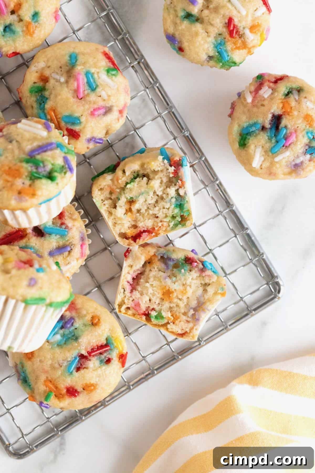 Freshly baked confetti mini muffins cooling on a metal rack, their vibrant sprinkles shining.