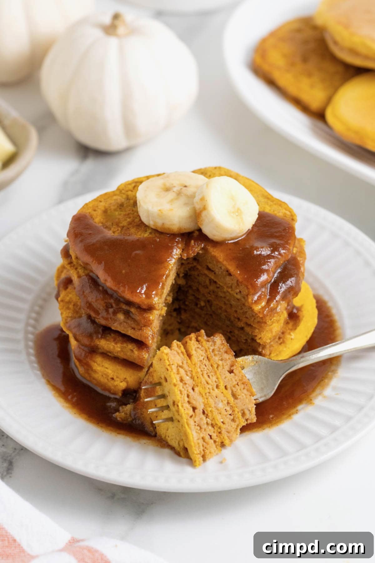 Autumn Pumpkin Banana Pancakes with Pumpkin Spice Drizzle 3 A stack of four pumpkin banana pancakes with a bite taken out.