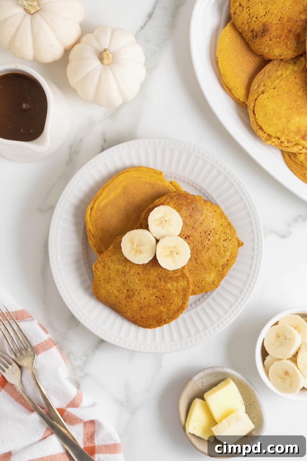 Autumn Pumpkin Banana Pancakes with Pumpkin Spice Drizzle 4 Three pumpkin banana pancakes on a white plate. There are three banana slices on the pancakes.