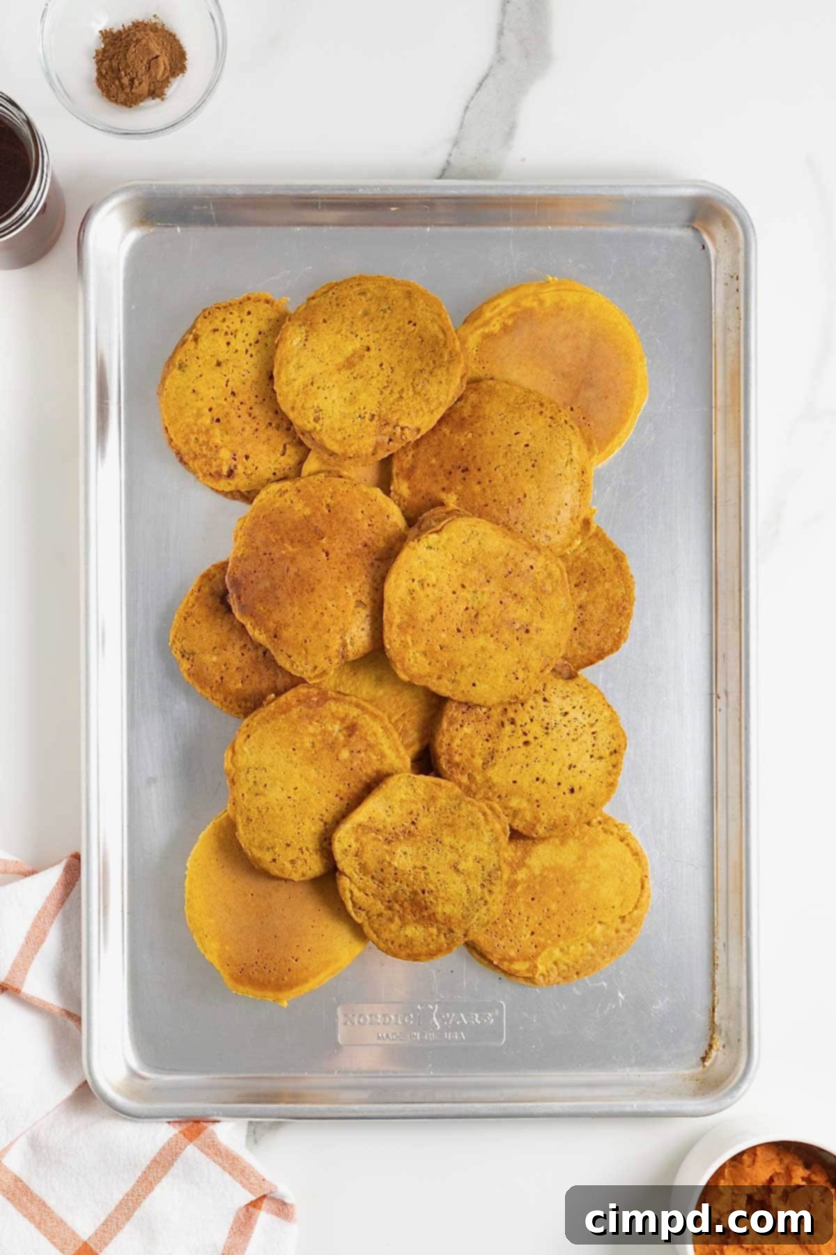 Autumn Pumpkin Banana Pancakes with Pumpkin Spice Drizzle 10 Pumpkin banana pancakes on an aluminum baking sheet.