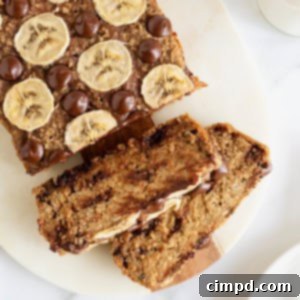 A loaf of banana bread garnished with banana slices and chocolate chips on a white cutting board.