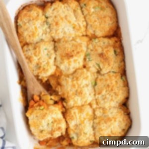 A white casserole dish of buffalo chicken biscuit bake with a wooden spoon in it.