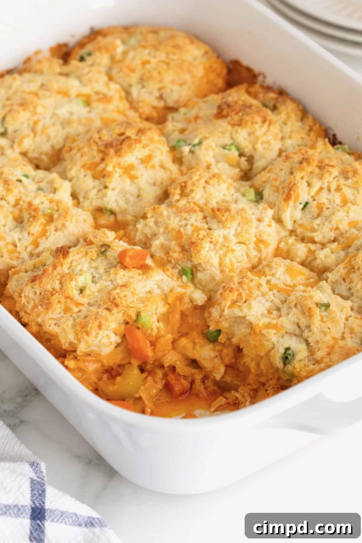 A white casserole dish of Buffalo Chicken Biscuit Bake with a serving already taken, showing the rich filling and soft biscuit topping.