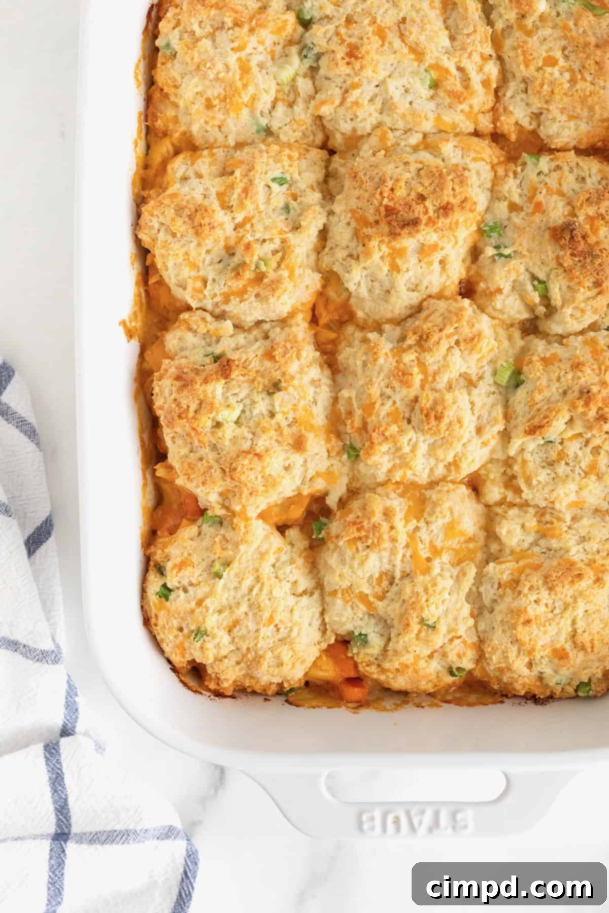 A white casserole dish filled with Buffalo Chicken Casserole, topped generously with golden-brown biscuits, ready to be served.