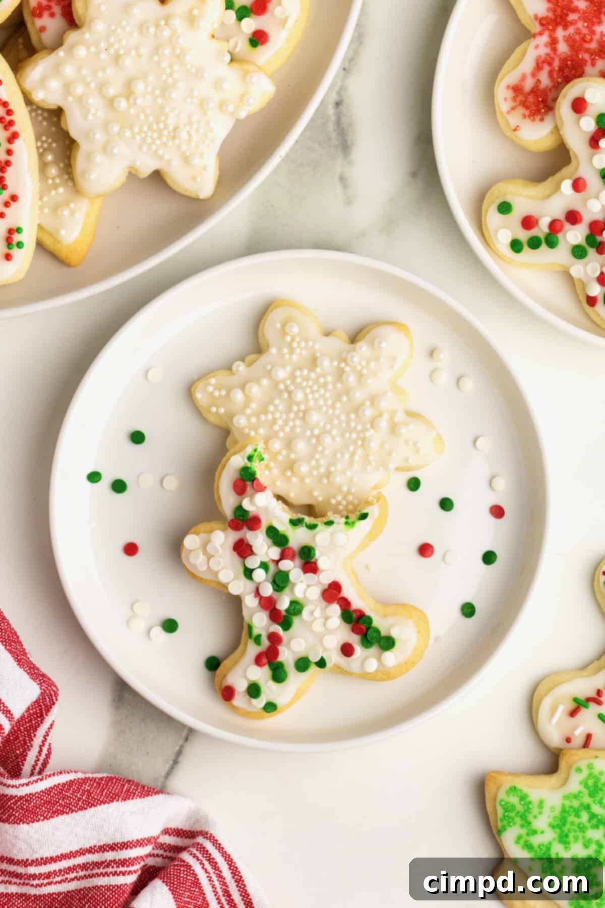 A white plate with two ice sugar cookies on it. One is a star with shite sprinkles and the other is a gingerbread man shape with red, white and green sprinkles. The gingerbread man has a bite out of it.