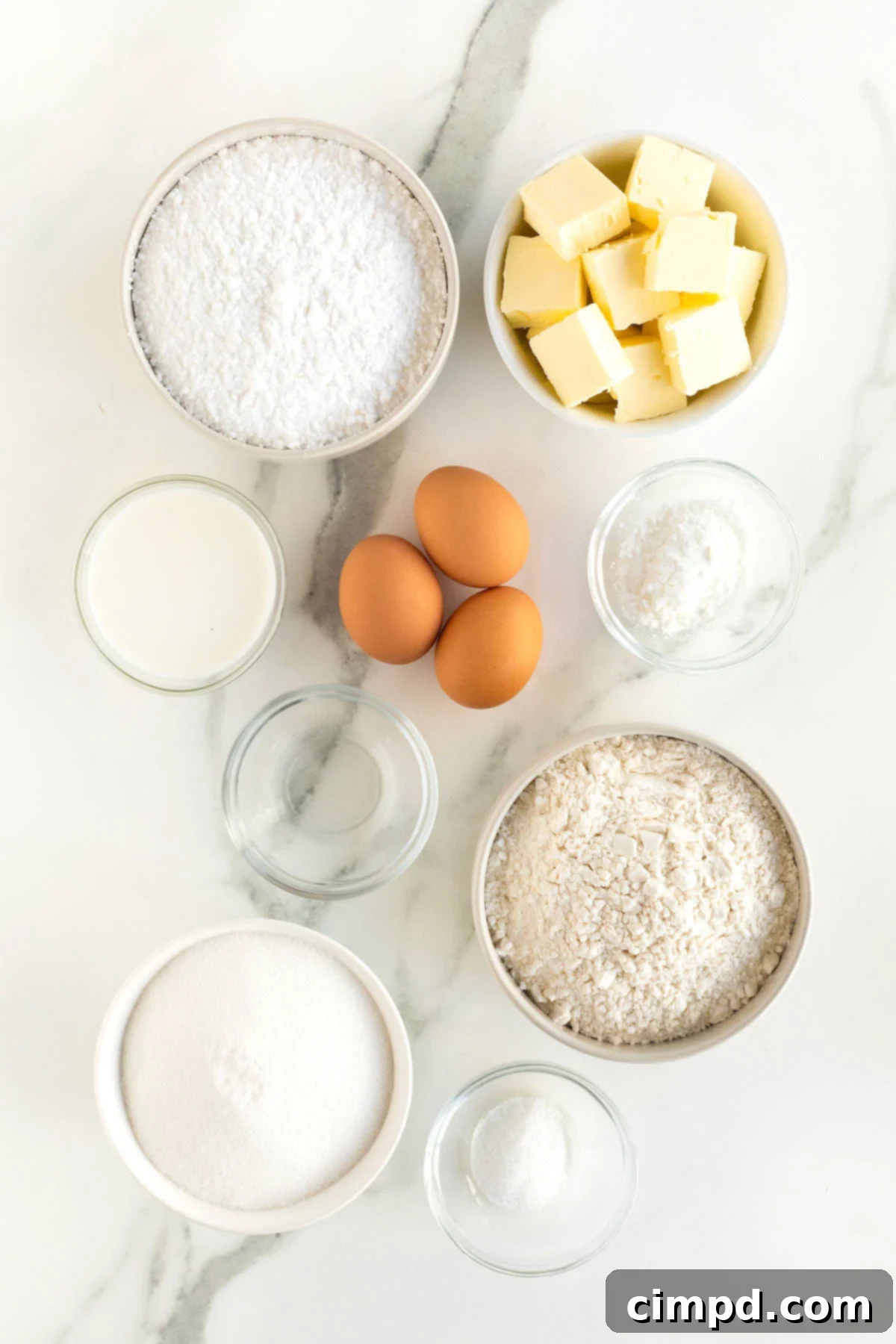 Ingredients to make sugar cookies in small glass dishes on a white marble counter.
