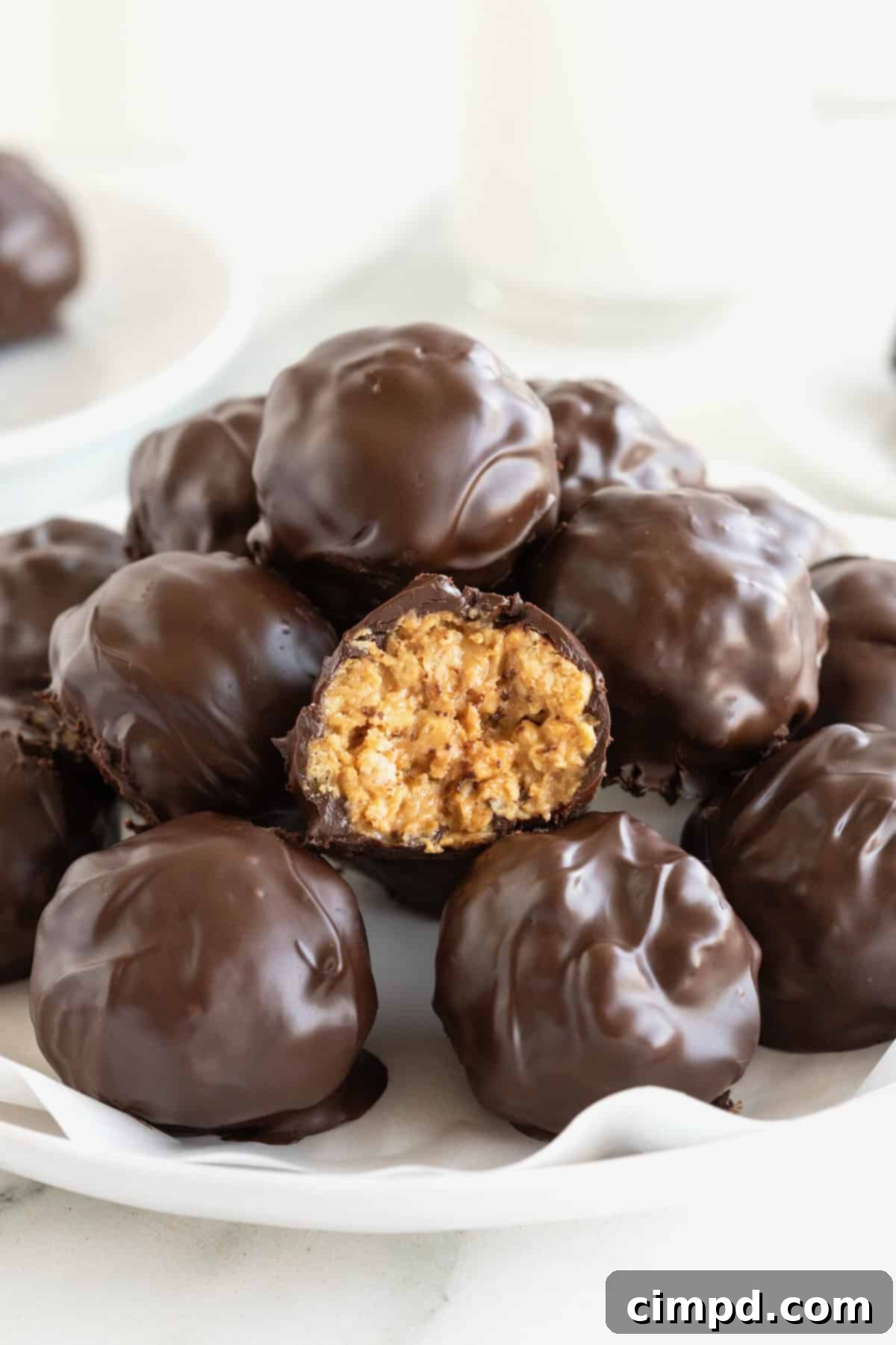 A pile of dark chocolate peanut butter balls in a parchment lined white serving dish, perfectly crafted and ready to be enjoyed.