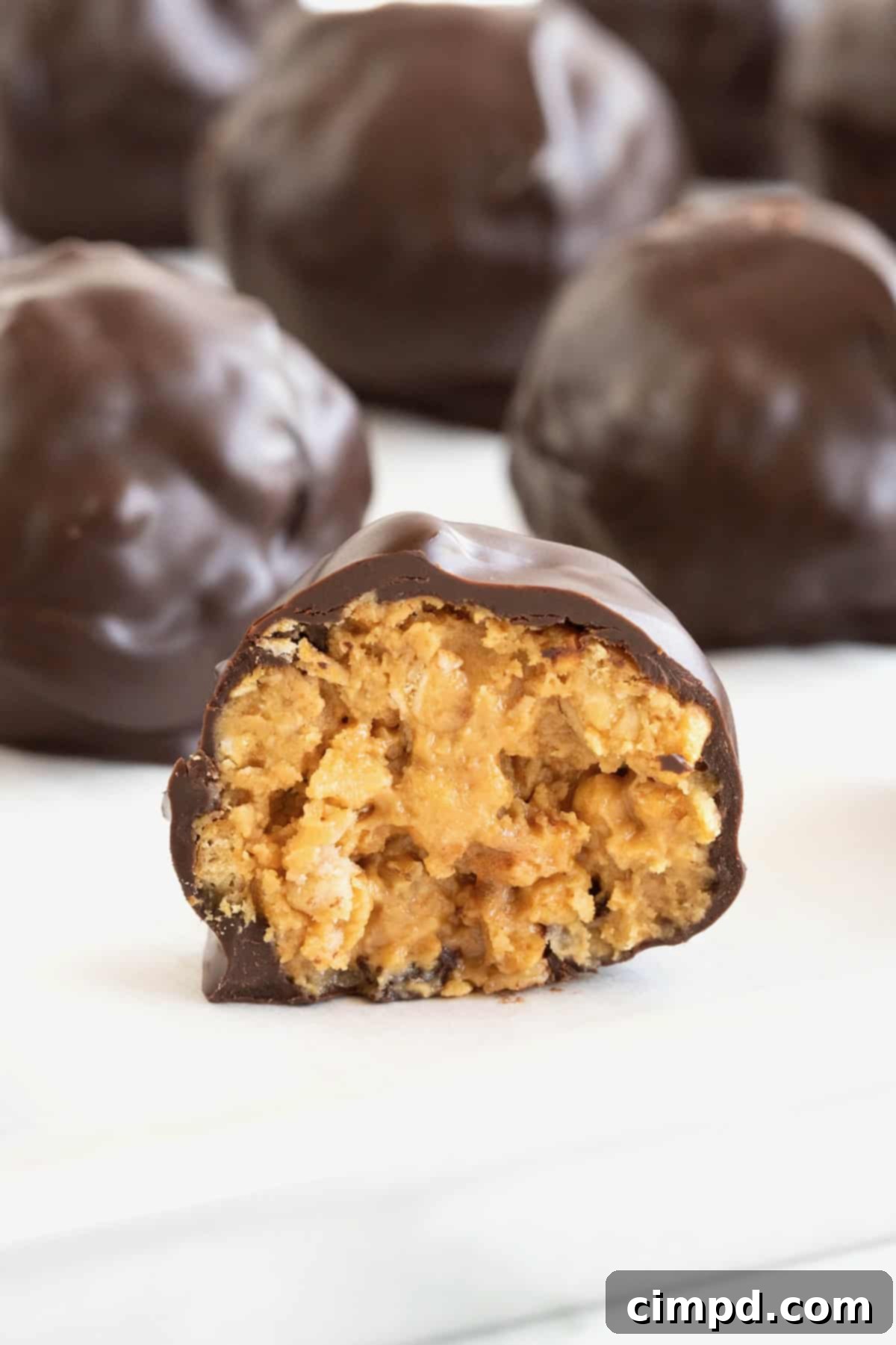 A dark chocolate covered peanut butter ball cut in half on a piece of parchment, revealing the crunchy granola and creamy peanut butter filling.