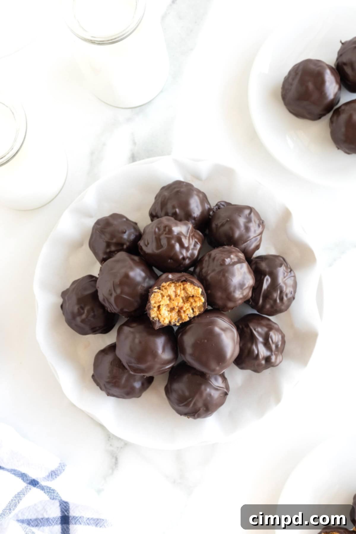 A pile of dark chocolate peanut butter balls in a parchment lined white serving dish, ready to be served or stored.