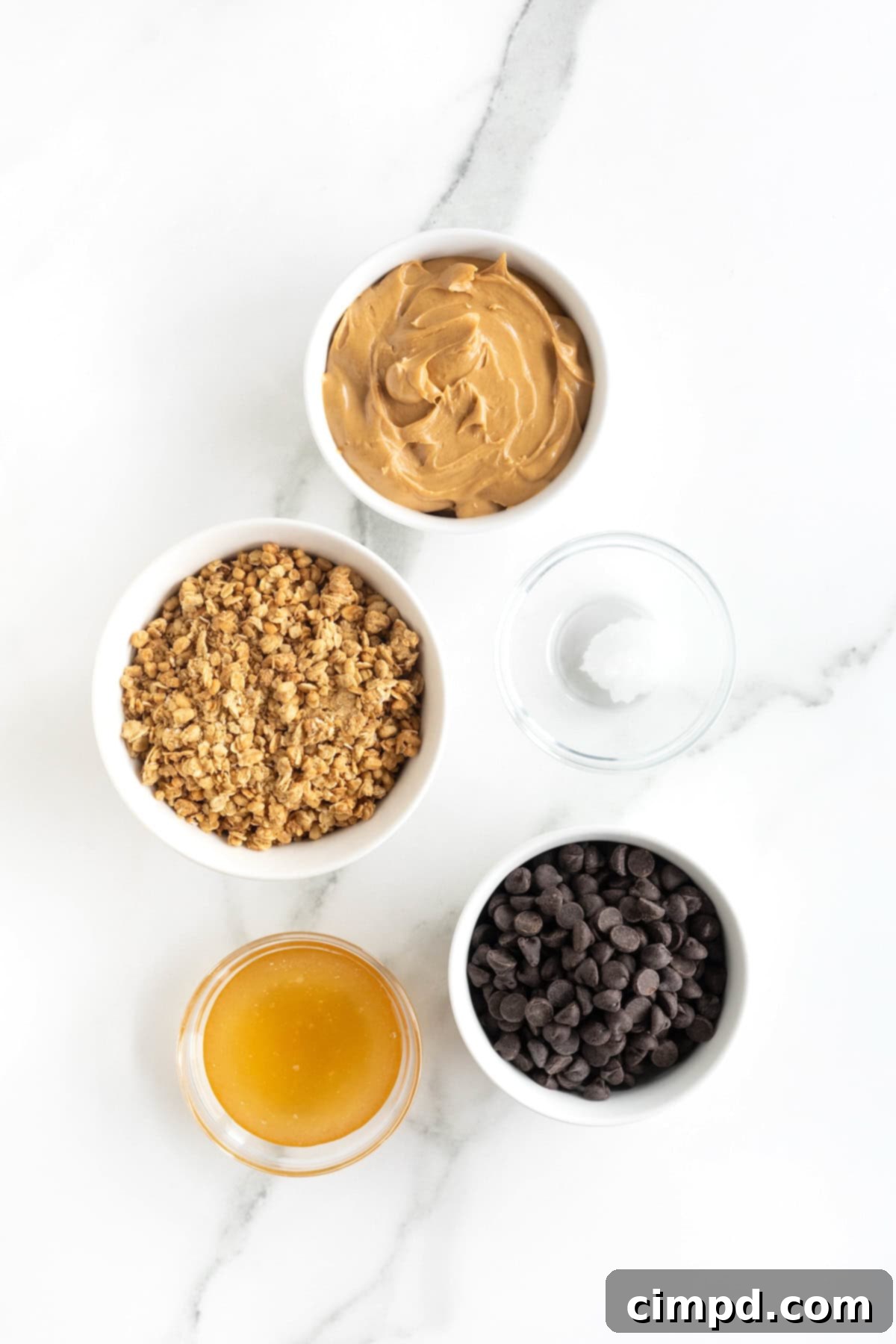 Ingredients to make healthy peanut butter balls in small glass dishes on a white marble counter, neatly arranged.