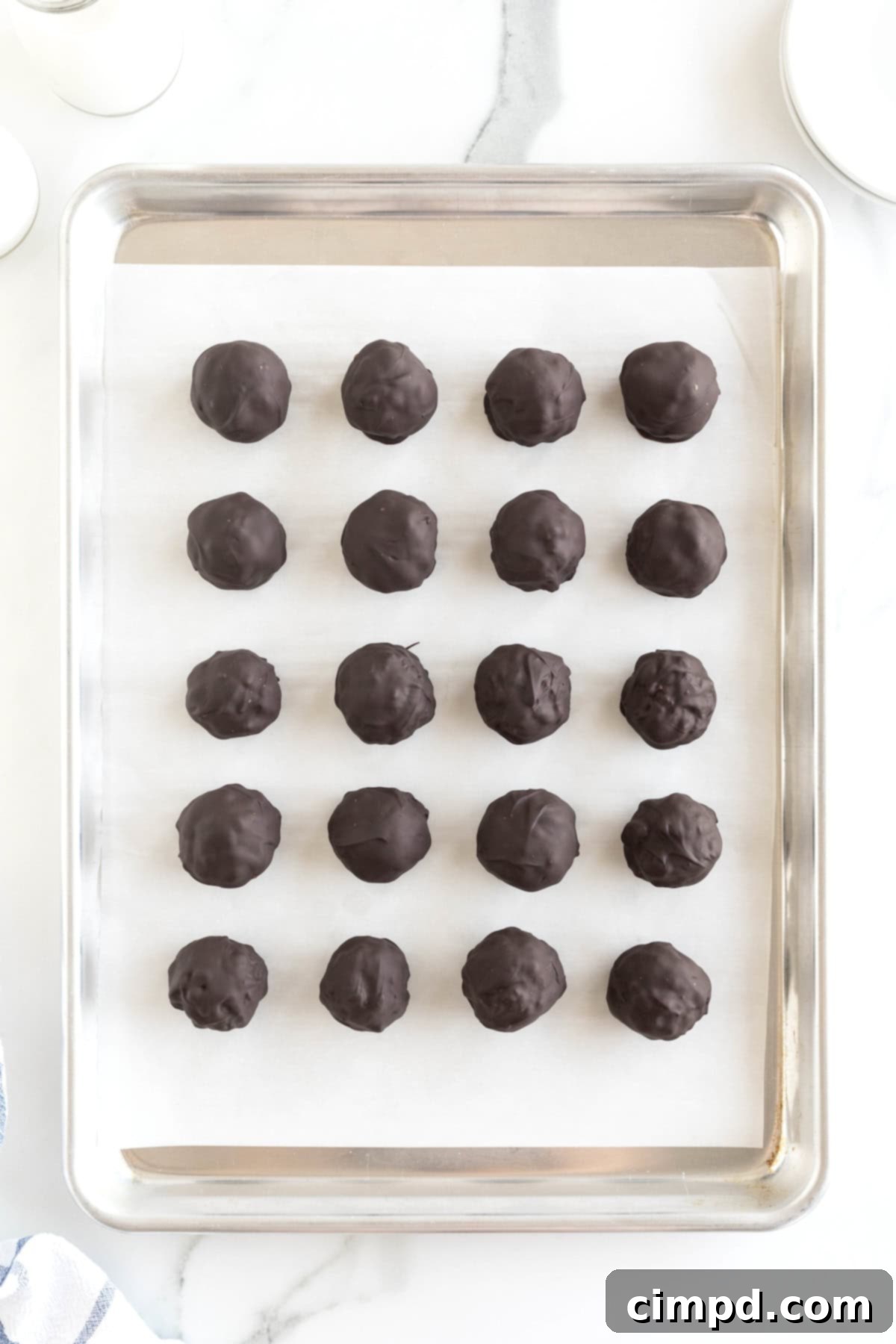20 Chocolate covered peanut butter balls on a parchment lined rimmed baking sheet, perfectly set and ready for storage.
