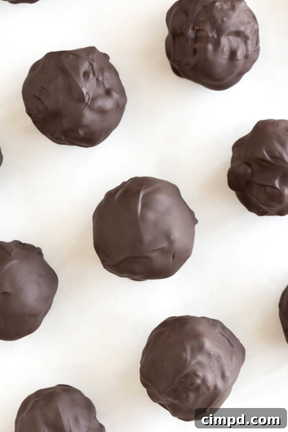 Seven dark chocolate peanut butter balls on a piece of parchment, showcasing their smooth chocolate coating.