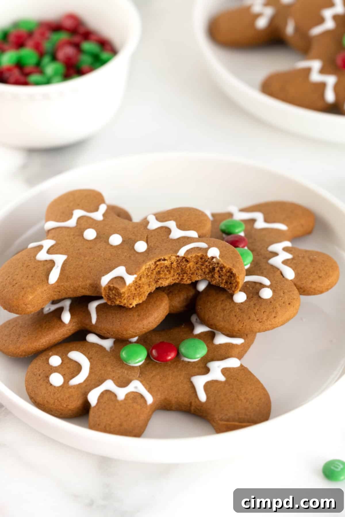Spiced Gingerbread Delights 3 A pile of gingerbread men cookies on a white plate. the top cookie has a bite out of it, showing the chewy texture of the cookie.