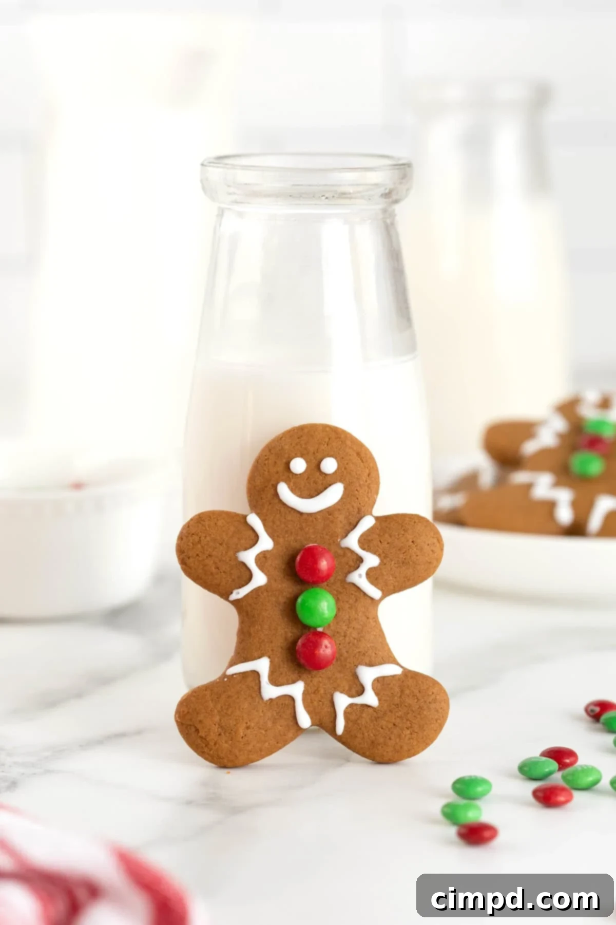 Spiced Gingerbread Delights 4 A gingerbread man cookie with green and red M&M buttons leaning against a carafe of milk.