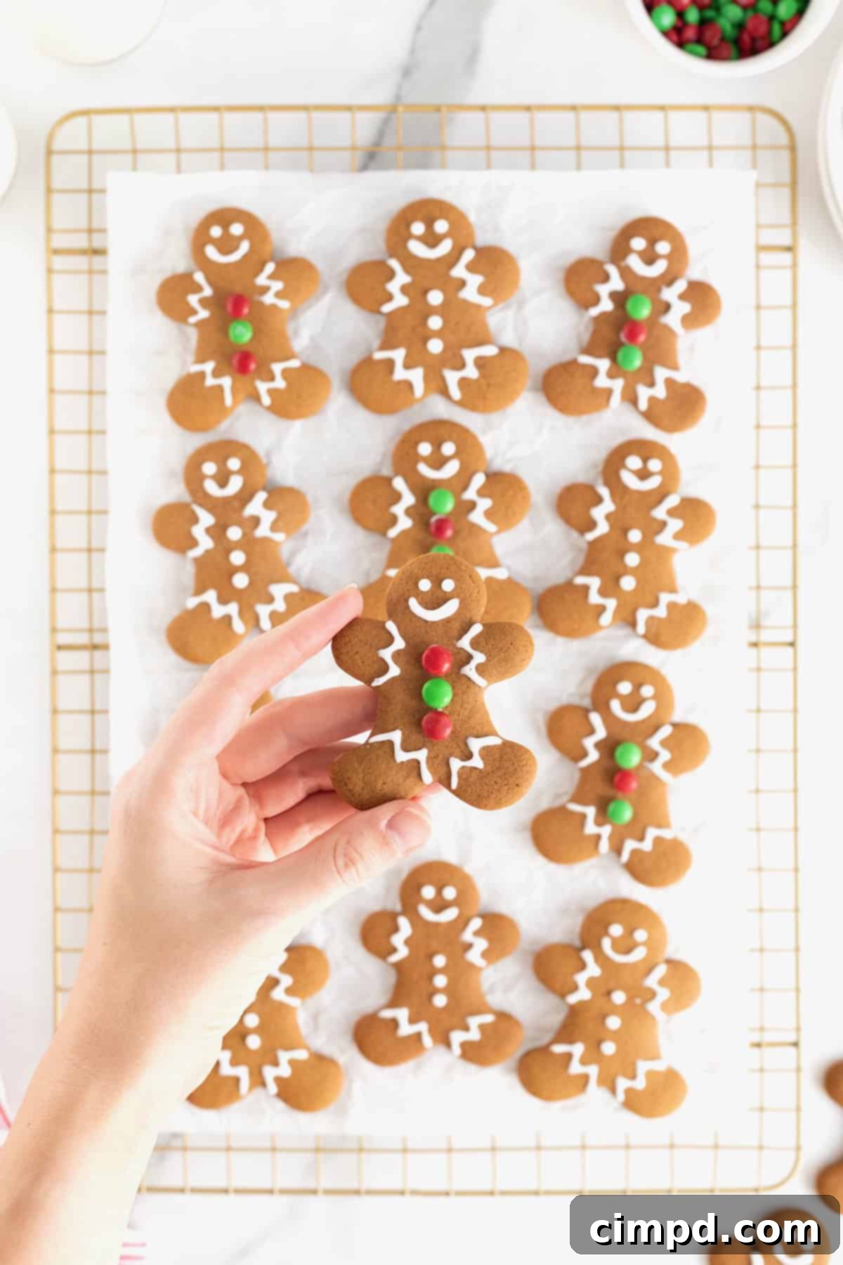 Spiced Gingerbread Delights 5 A hand holding a gingerbread man cookie over a parchment lined cooling rack filled with more cookies.