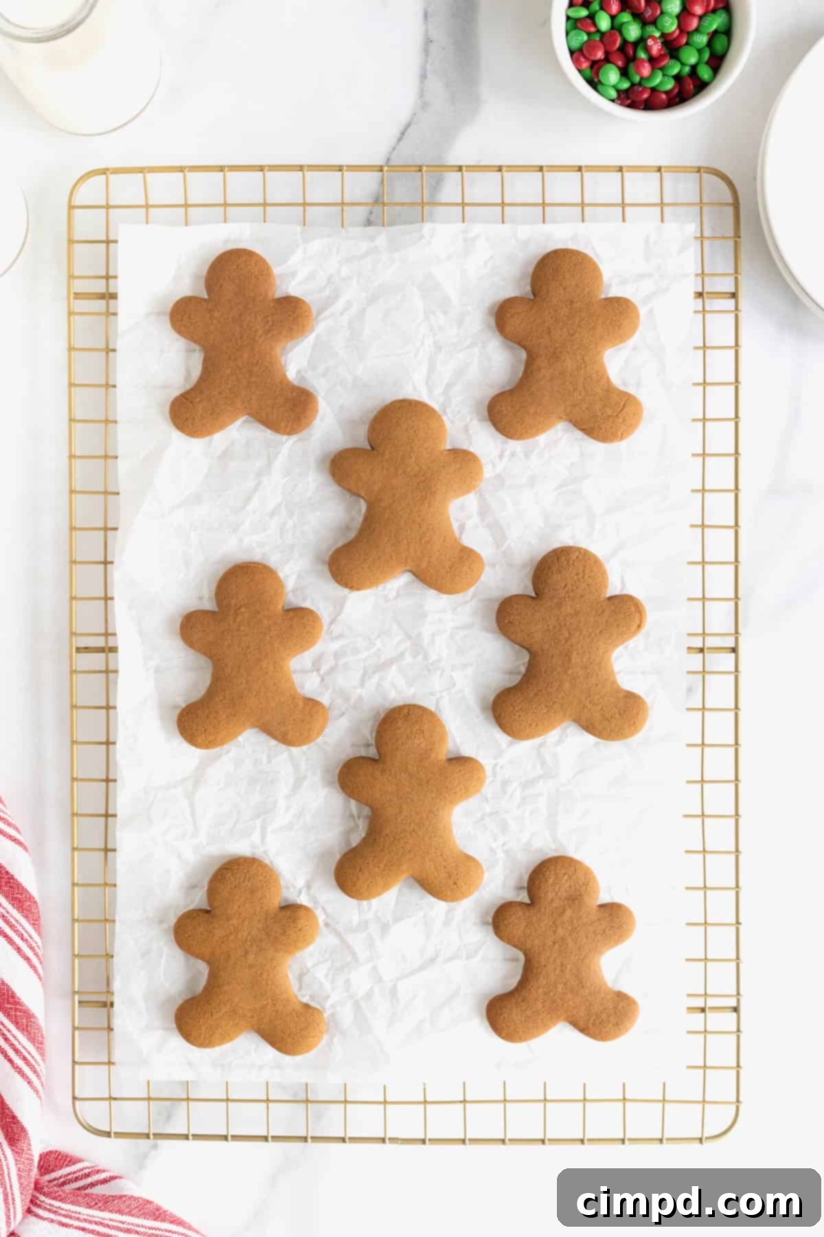 Spiced Gingerbread Delights 9 Eight undecorated gingerbread men cookies on a parchment lined gold toned cooling rack.