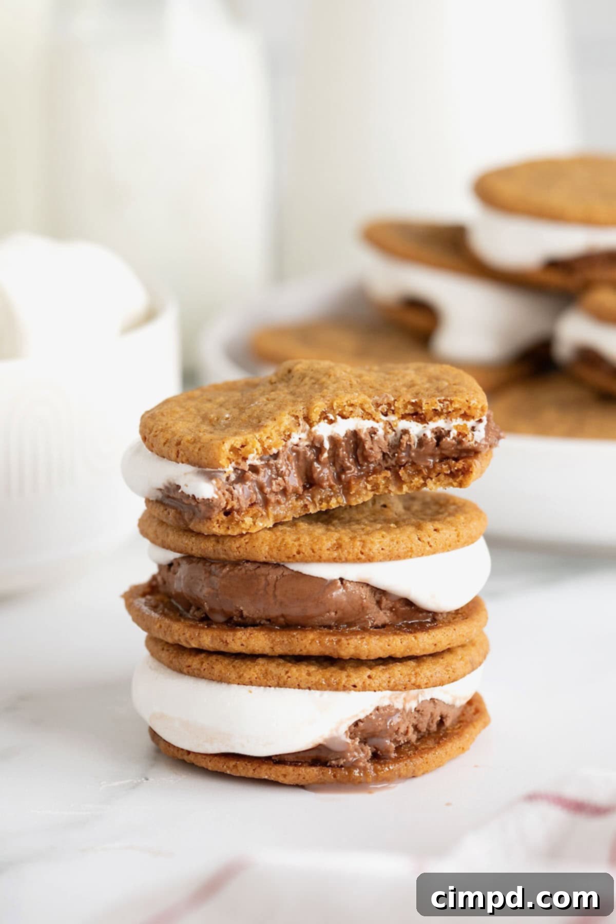 A stack of three s'mores ice cream sandwiches on a white marble surface. The top ice cream sandwich has a bite out of it.