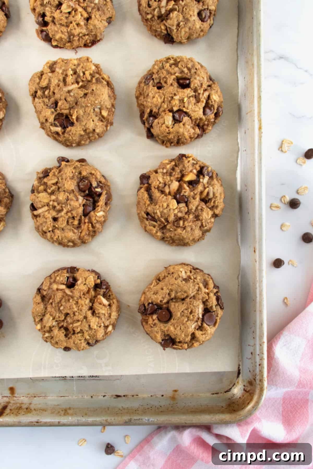 Eight breakfast cookies with chocolate chips on a parchment lined aluminum baking sheet.