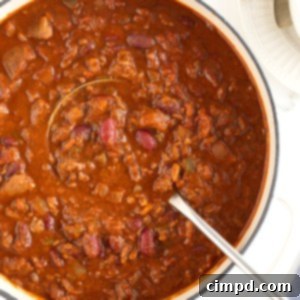 The Gold Standard Chili 13 A Dutch oven filled with the best homemade chili on a white background, featuring a metal ladle, ready to be served. A perfect representation of a hearty and comforting meal.