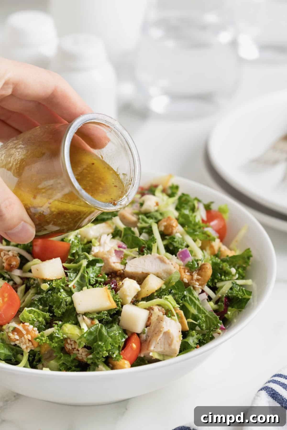 Quick 5-Minute Lunch Salad 6 Dressing in a small glass carafe being poured onto a salad in a white bowl.