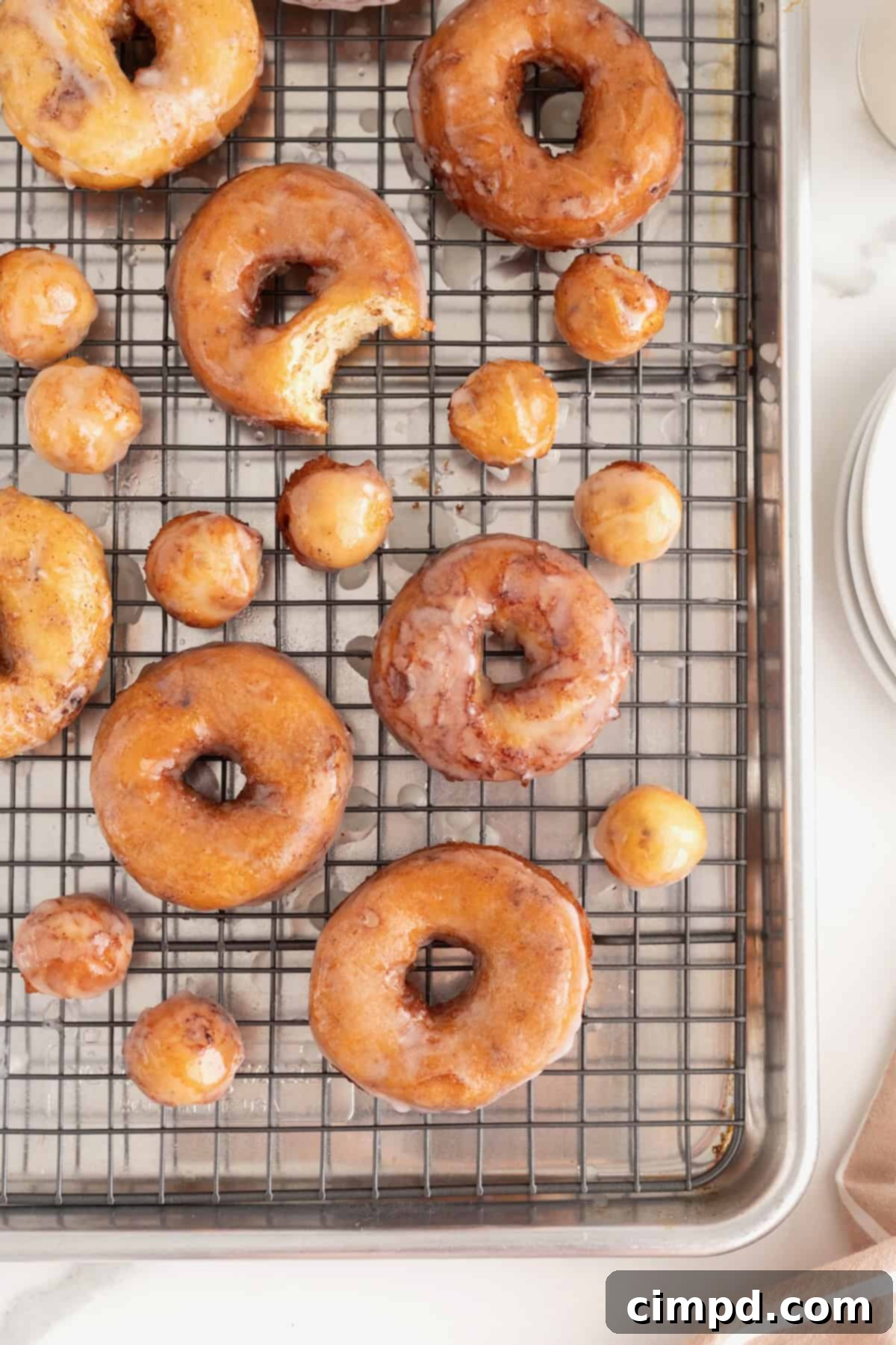 Shortcut Cinnamon Roll Donuts 2 Freshly fried cinnamon roll donuts cooling on a metal rack, glistening with sweet cream cheese glaze.