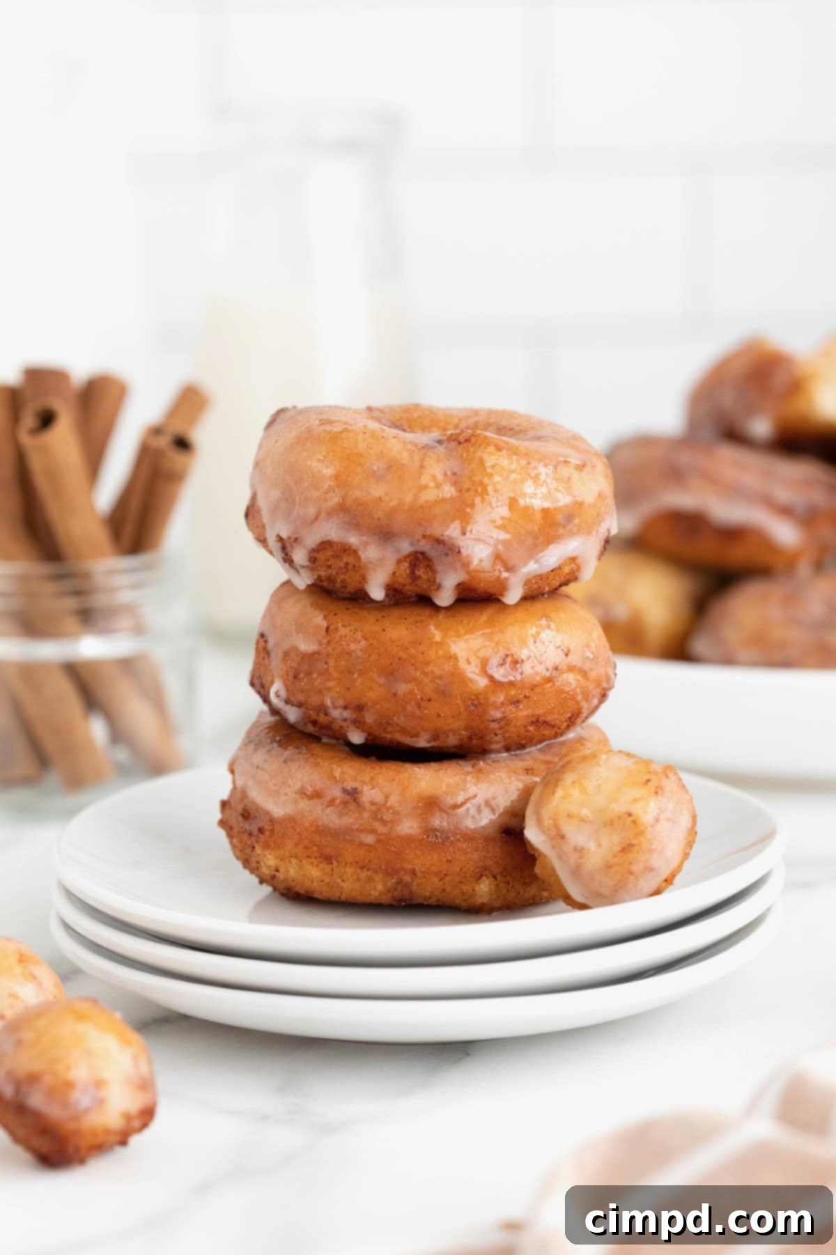 Shortcut Cinnamon Roll Donuts 3 Three perfectly stacked cinnamon roll donuts on white plates, with a golden donut hole alongside.