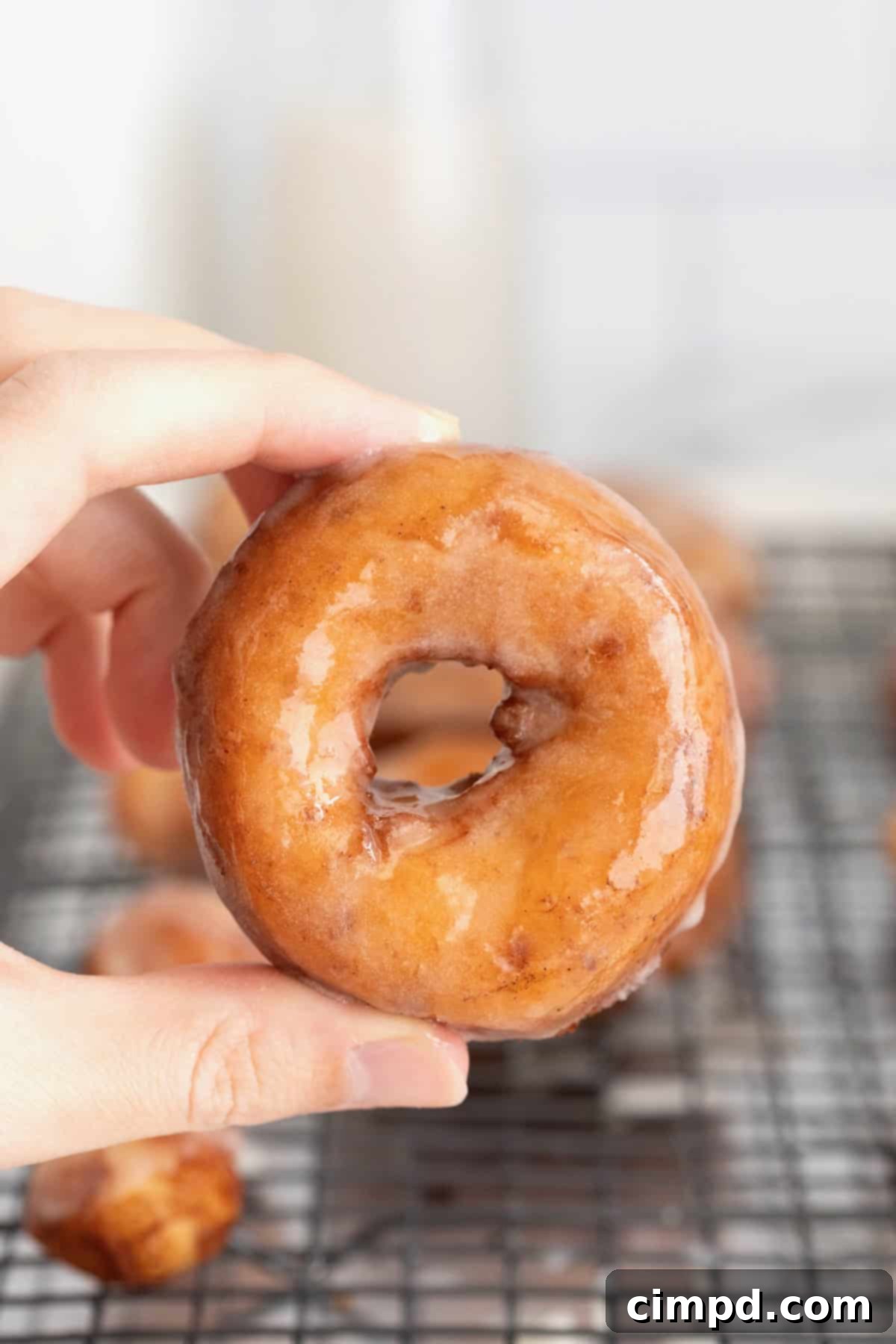 Shortcut Cinnamon Roll Donuts 4 A hand reaching for a warm, glazed cinnamon roll donut, showcasing its inviting texture.