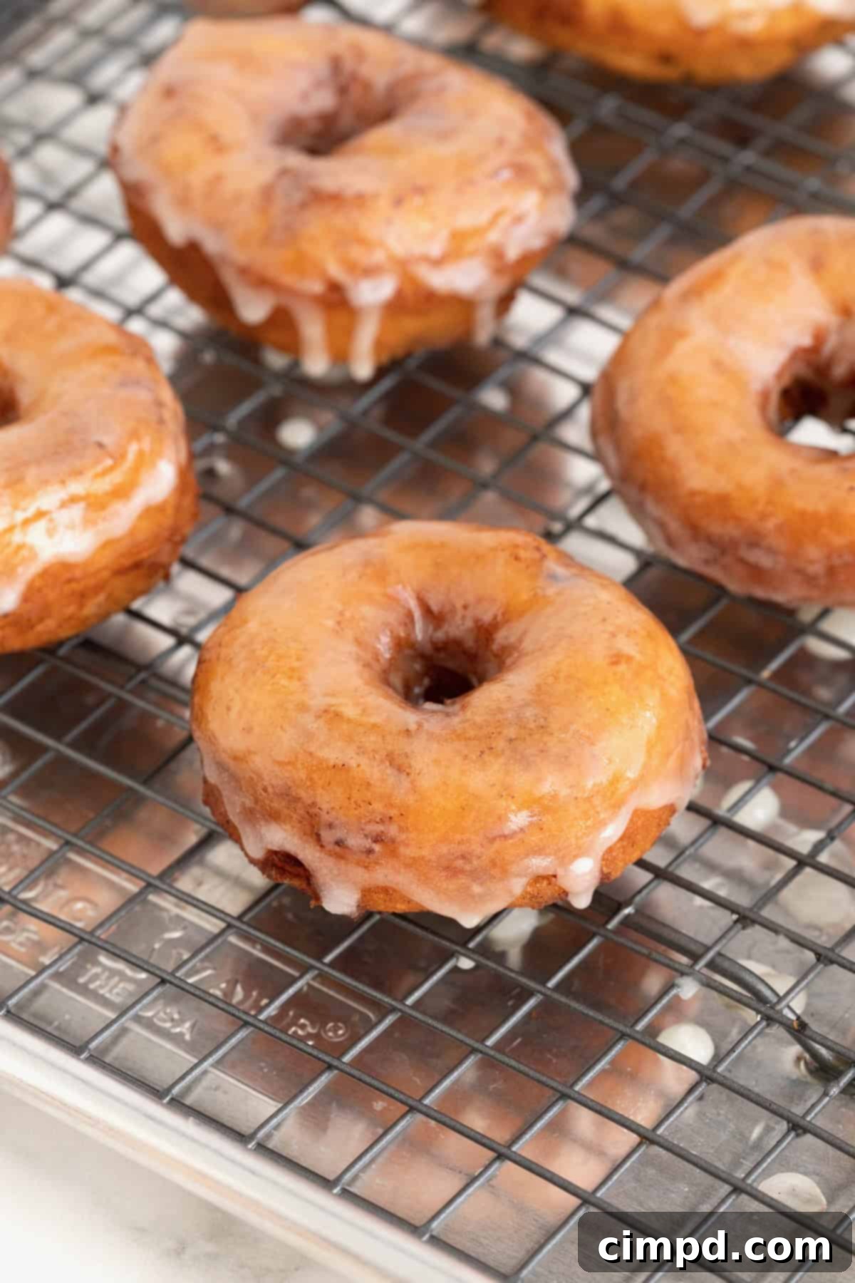 Shortcut Cinnamon Roll Donuts 9 A batch of glazed cinnamon roll donuts resting on a cooling rack over a rimmed baking sheet.