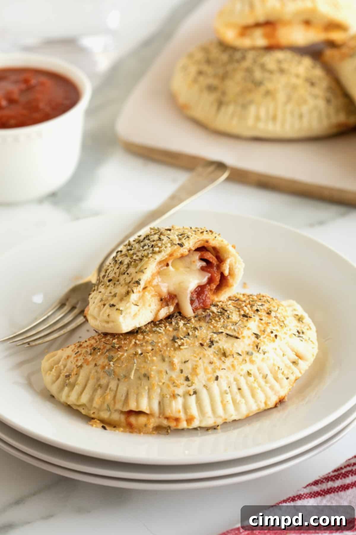 A mini pepperoni calzone and a half eaten calzone on a white plate with a fork. 