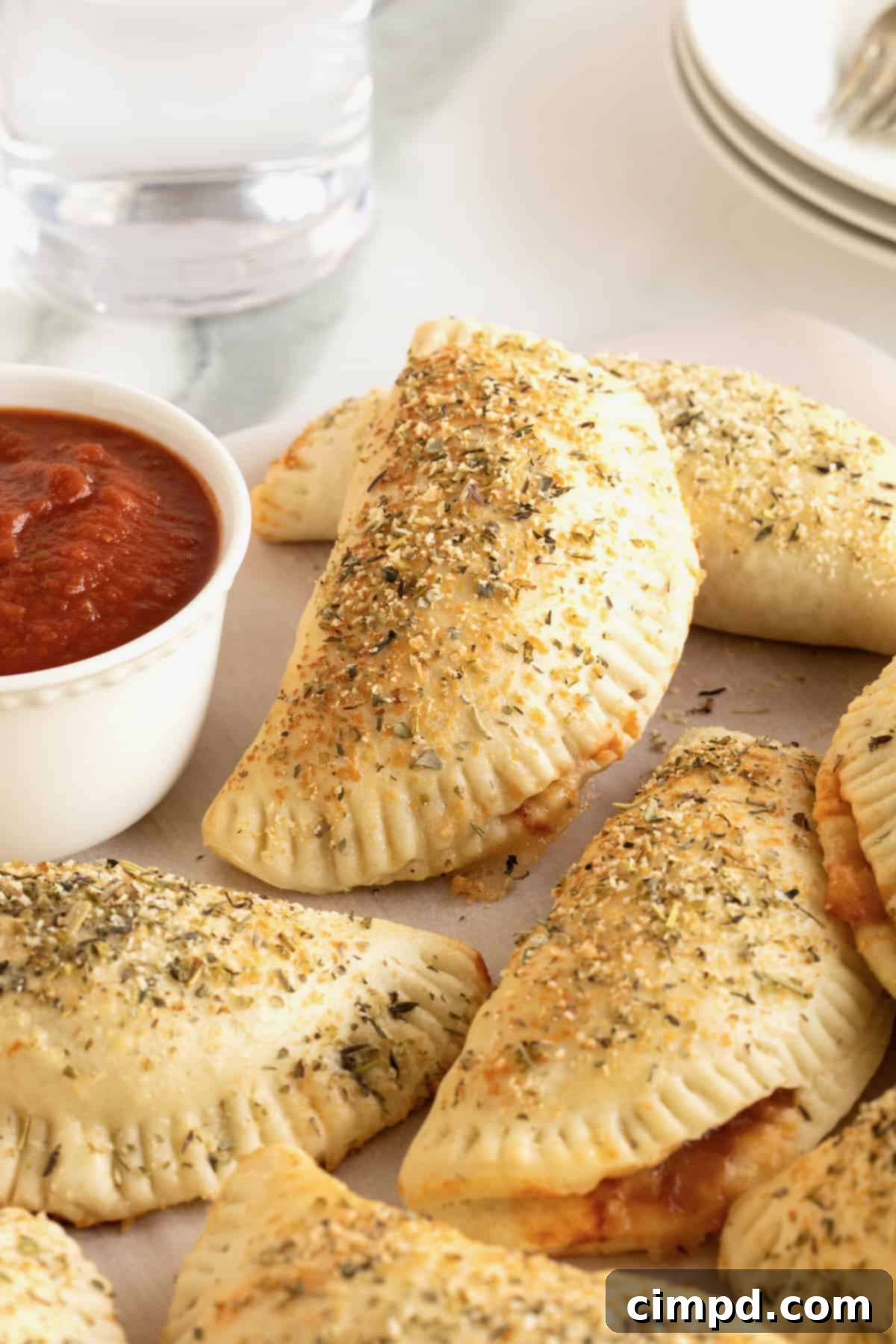 Five mini calzones on a white plate next to a small dish of marinara sauce.